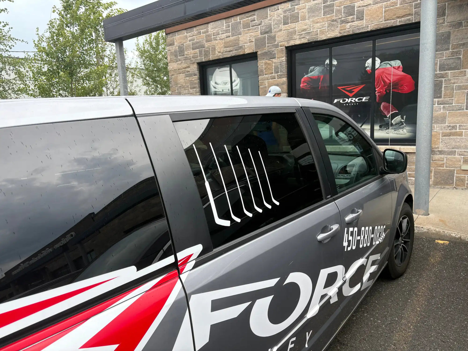Minivan gris avec des autocollants de marque 'force' en rouge et blanc audacieux.